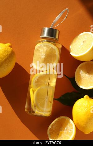 Acqua di limone in bottiglia, frutta fresca e foglie su fondo marrone, stendere piano Foto Stock