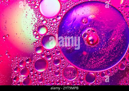 Forme circolari di olio in acqua con evidenziazioni rosa Foto Stock