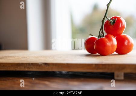 Pomodori rossi maturi su un tagliere di legno di fronte a una luminosa finestra della cucina. Sfondo con breve profondità di campo e spazio per il testo. Foto Stock