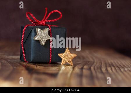 Presente per Natale con nastro rosso due stelle in oro e argento di fronte a uno sfondo scuro Foto Stock