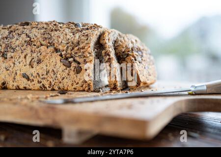 Pane multigrano appena tagliato su una superficie in legno con un coltello. Primo piano di fronte alla finestra luminosa. Foto Stock