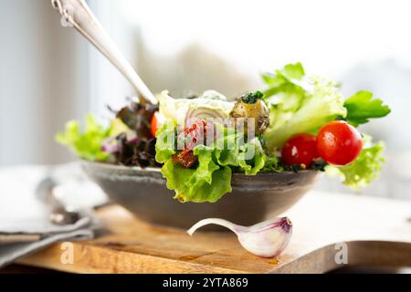 Insalata verde fresca in un recipiente in ceramica con pomodoro, cipolle e olive su tagliere in legno. Concetto di nutrizione sana per il fitness e la dieta primaverile. Primo piano. Foto Stock