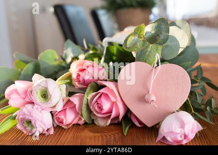 Bouquet di rose rosa con ranunculus e cuore rosa su un tavolo di legno per i saluti della mamma. Foto Stock
