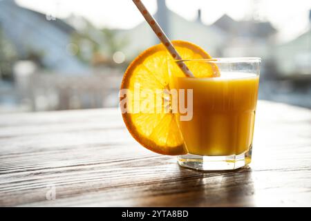 Bicchiere di succo d'arancia appena spremuto con una fetta di arancia e cannuccia da bere su un tavolo rustico in legno. Primo piano. Foto Stock