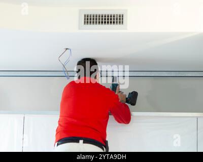 Il lavoratore di cartongesso installa una parete di cartongesso sugli armadi della cucina per coprire il tubo di estrazione del cofano Foto Stock