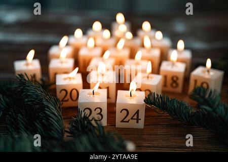 Calendario dell'Avvento fatto di ventiquattro candele in fiamme. Candele fatte in casa con cera d'api naturale. Disposizione a forma di albero di natale su un tavolo di legno scuro con rami di abete. Sfondo natalizio con breve profondità di campo. Foto Stock