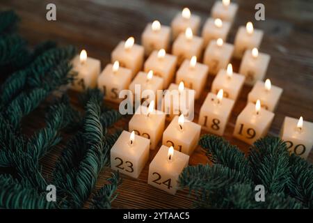 Calendario dell'Avvento fatto di ventiquattro candele in fiamme. Candele fatte in casa con cera d'api naturale. Disposizione a forma di albero di natale su un tavolo di legno scuro con rami di abete. Sfondo natalizio con breve profondità di campo. Foto Stock