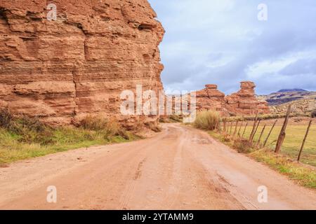 Una strada sterrata si snoda attraverso un canyon roccioso. La strada è fangosa e il cielo è nuvoloso. La scena è un po' desolata e desolata Foto Stock