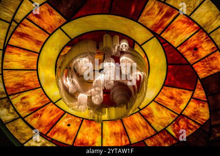 Un lampadario dal design giallo e rosso pende dal soffitto. Il lampadario è realizzato in vetro e ha un design a spirale. La luce del chandeli Foto Stock