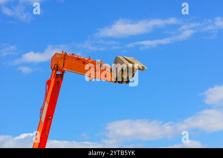 Una benna arancione dell'escavatore appesa in alto contro il cielo. Foto Stock