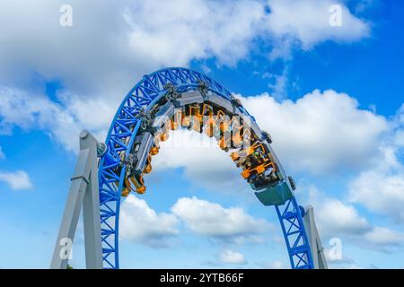Carrello delle montagne russe con persone che lo guidano passa attraverso un giro capovolto su uno sfondo di cielo blu e nuvole. Foto Stock