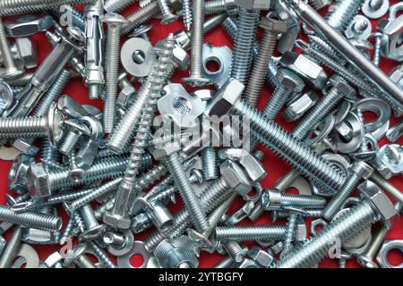 Diversi bulloni filettati, viti e dadi cromati su sfondo rosso Foto Stock