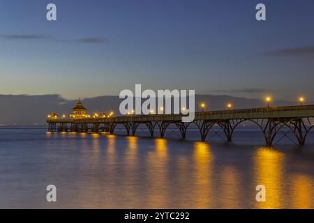 Clevedon Pier in prima serata con mare calmo con il suo fulmine che si riflette sul mare con cieli azzurri Foto Stock