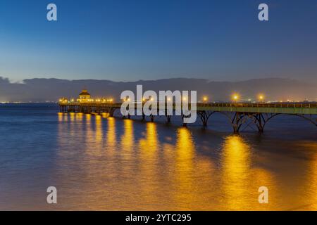 Clevedon Pier in prima serata con mare calmo con il suo fulmine che si riflette sul mare con cieli azzurri Foto Stock