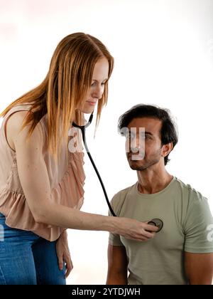 Giovane medico europeo in visita a un uomo asiatico. Ascoltando il suo petto con lo stetoscopio. Foto Stock