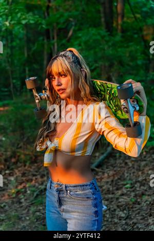 Una radiosa giovane donna messicana americana con capelli bicolore marrone scuro e caramello sorride calorosamente. Le piace una giornata estiva di sole al parco, sullo skateboard Foto Stock