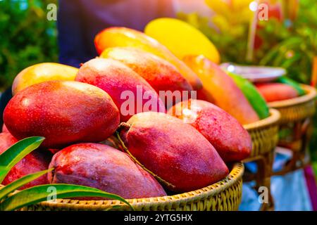 Grande mango rosso con rami e foglie alberelli disposti ordinatamente su una piccola bancarella di frutta nel mercato dei frutti tropicali Foto Stock