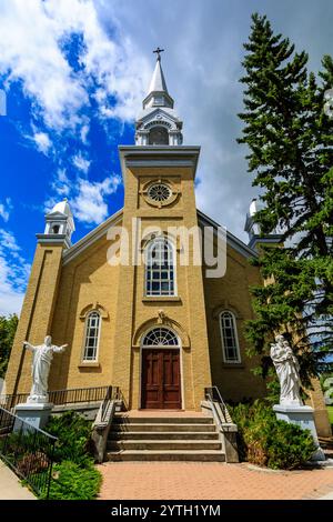 Una grande chiesa con un campanile e una croce in cima. La chiesa è circondata da un giardino e presenta una statua di Gesù Cristo sui gradini Foto Stock