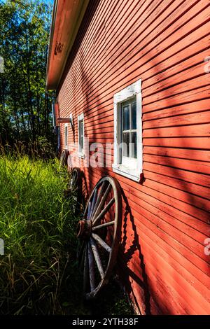 Un fienile rosso con una ruota laterale. La ruota è vecchia e arrugginita. Il fienile è circondato da alberi Foto Stock