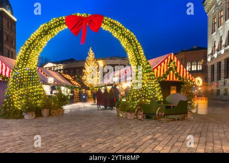 Ingresso al mercato di Natale nella vecchia riga con un arco illuminato adornato da un grande arco rosso, bancarelle festose e un albero di Natale illuminato sotto la t Foto Stock