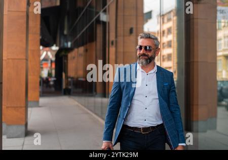 Un uomo maturo e felice in abiti eleganti che camminano per la strada della città. Foto Stock