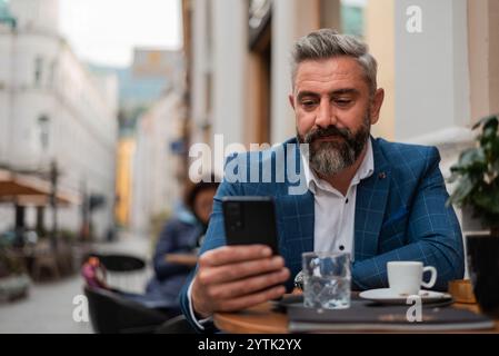Un uomo d'affari maturo che scrive al telefono in un bar del ristorante durante una pausa caffè. Foto Stock