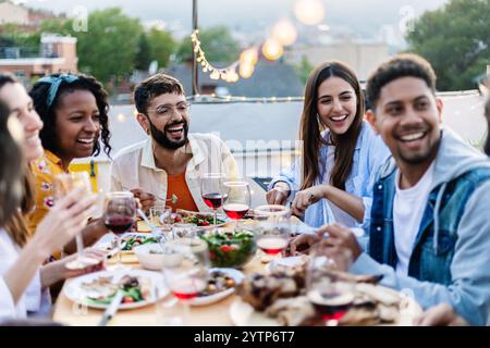 Un gruppo di amici felice si gusta la cena al barbecue in estate sulla terrazza di casa Foto Stock