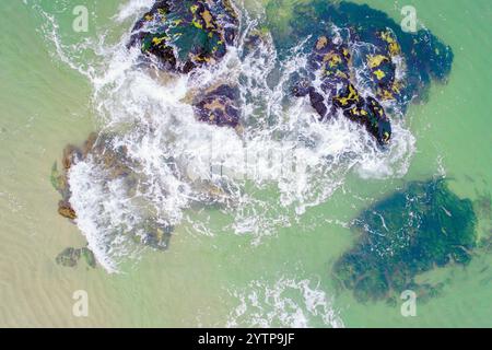 onde che si infrangono su rocce muschiate sulla riva di una spiaggia, vista dall'alto con drone, Foto Stock