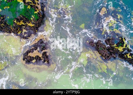 onde che si infrangono su rocce con muschio sulla riva di una spiaggia, vista zenithal con drone Foto Stock