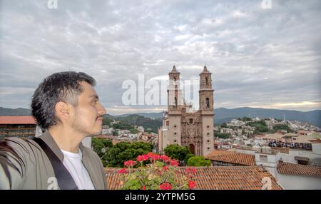 Catturando l'essenza di Taxco de Alarcon, questo momento mostra una persona che ammira la suggestiva architettura coloniale e i vivaci fiori nelle vicinanze. Foto Stock