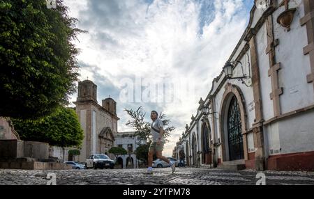 Una persona fa jogging lungo le affascinanti strade acciottolate di Taxco de Alarcon, Guerrero, circondate dall'architettura coloniale. Il cielo atmosferico è pieno Foto Stock