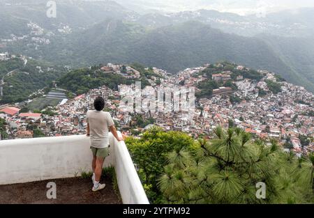 Un uomo guarda il paesaggio mozzafiato di Taxco de Alarcon a Guerrero, in Messico. Sotto di lui, i vivaci edifici della città si annidano tra le colline, Foto Stock
