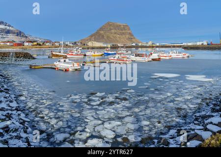 Porto di Grundarfjörður con barche da pesca e ghiaccio galleggiante sotto il cielo blu, Kirkjufell sullo sfondo, Islanda invernale. Foto Stock