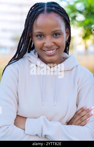 Giovane donna sorridente con i capelli intrecciati che indossa una felpa con cappuccio all'aperto. Verticale Foto Stock