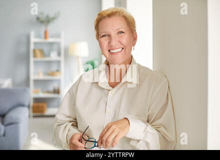 Ritratto di una donna matura in salotto e con gli occhiali in mano. Foto Stock