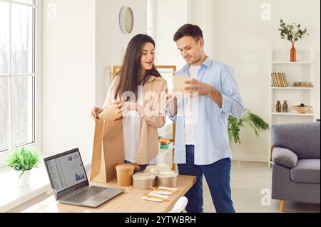Giovane uomo e donna felice che disimballano i pacchetti alimentari con il cibo in scatole di cartone da ordine online. Foto Stock