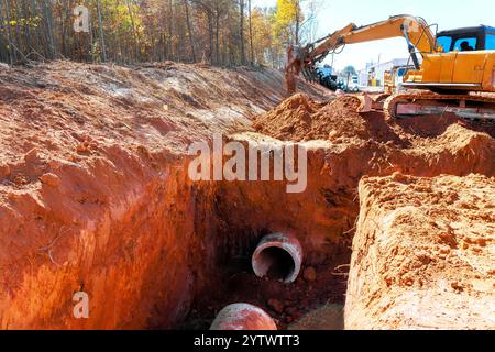 L'escavatore pesante lavora per scavare fossati per nuove tubazioni circondati da cantieri residenziali Foto Stock