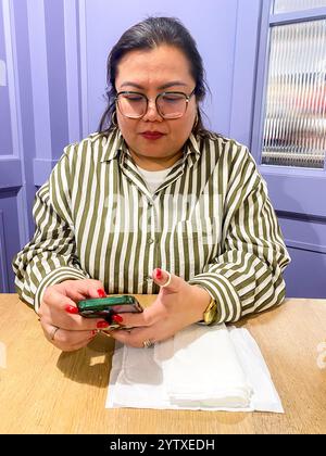 Una signora si siede a un tavolo in un ristorante con il suo cellulare. Foto Stock