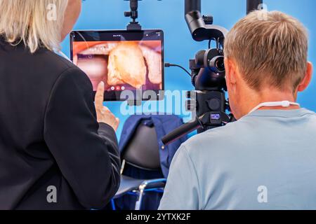 Un uomo guarda nel binocolo di un microscopio dentale. Davanti a lui c'è un monitor con un'immagine di una mascella e un dente Foto Stock