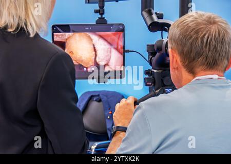 Un uomo guarda nel binocolo di un microscopio dentale. Davanti a lui c'è un monitor con un'immagine di una mascella e un dente Foto Stock