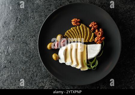 Formaggio cremoso Camembert con olive, rosmarino e noci su un piatto nero. Vista dall'alto. Foto Stock