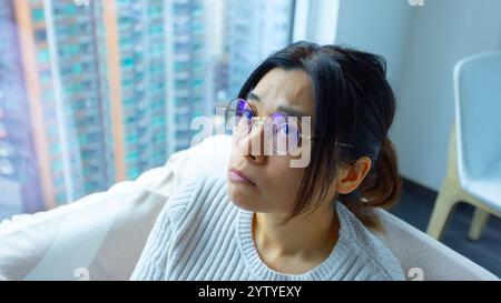 la donna guarda in alto e sente lo stress a casa, indossando gli occhiali Foto Stock