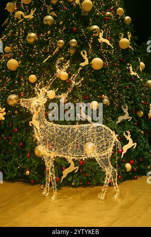 Renna dorata illuminata a LED con un grande albero di Natale sullo sfondo Foto Stock
