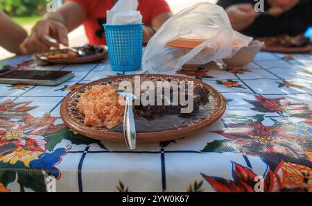 Un gruppo di persone si riunisce intorno a un tavolo colorato gustando un pasto tradizionale. L'attenzione è concentrata su un piatto caratterizzato da una ricca salsa scura che accompagna un mou Foto Stock