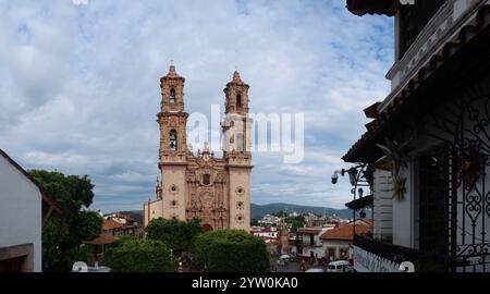 Una vista notevole della Chiesa di Santa Prisca a Taxco, Messico, che mostra la sua intricata architettura barocca. La vista cattura la vegetazione lussureggiante del Foto Stock