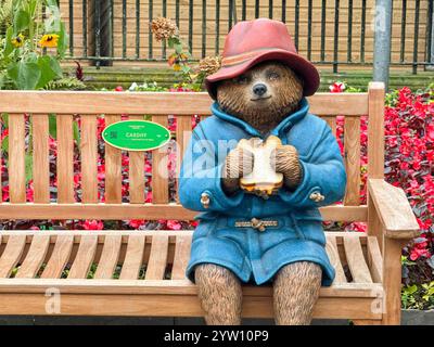 Cardiff, Galles - 10 novembre 2024: Modello di orso Paddington seduto su una panchina di legno in un parco pubblico nel centro di Cardiff Foto Stock