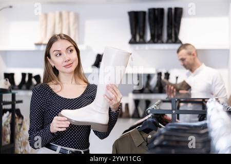 L'acquirente femminile guarda le calzature della nuova collezione e acquista un nuovo paio di stivali alti Foto Stock