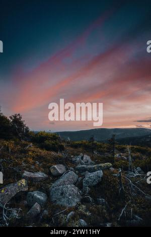 Si può ammirare un tramonto mozzafiato che si dispiega su una pittoresca collina rocciosa, con splendidi alberi che incorniciano la scena in primo piano Foto Stock