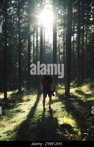 Un uomo sta passeggiando piacevolmente attraverso una splendida foresta, dove il sole splende luminoso e filtra tra i lussureggianti alberi verdi Foto Stock