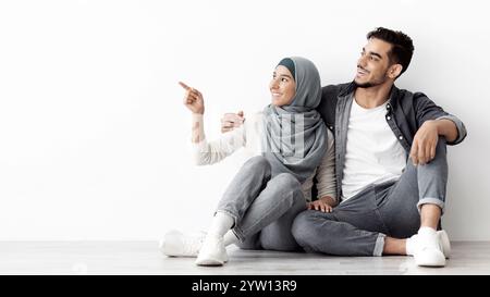 Donna sognante in hijab seduta sul pavimento con suo marito Foto Stock